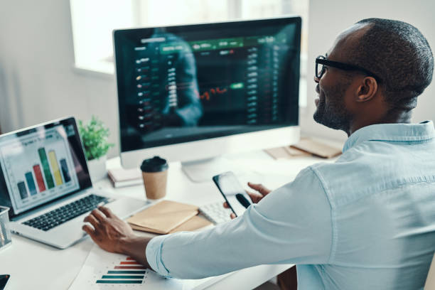 istockphoto-1194668332-612x612 Handsome young African man in shirt using computer and smiling while working in the office